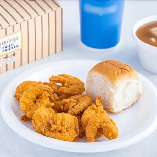 Fried shrimp and a dinner roll on a white plate, with a drink and gravy in the background.