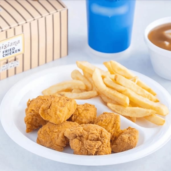 Fried chicken nuggets and french fries on a white plate with a drink and gravy.