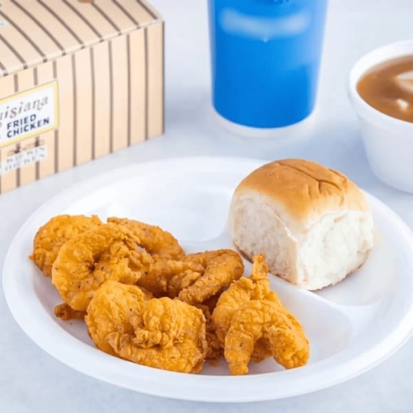 A plate of golden fried shrimp and a dinner roll, with a drink and sauce in the background.
