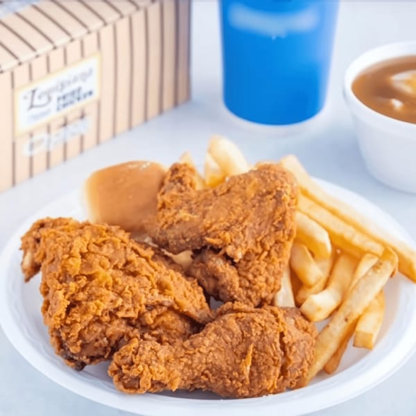 Crispy fried chicken pieces, golden french fries, and a dinner roll on a white plate.