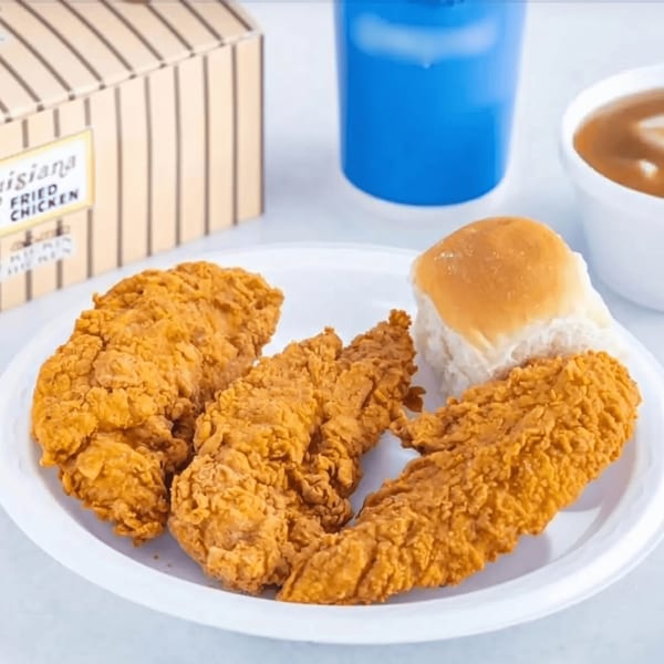 Three crispy fried chicken tenders, a dinner roll, gravy, and a blue drink cup on a white plate.