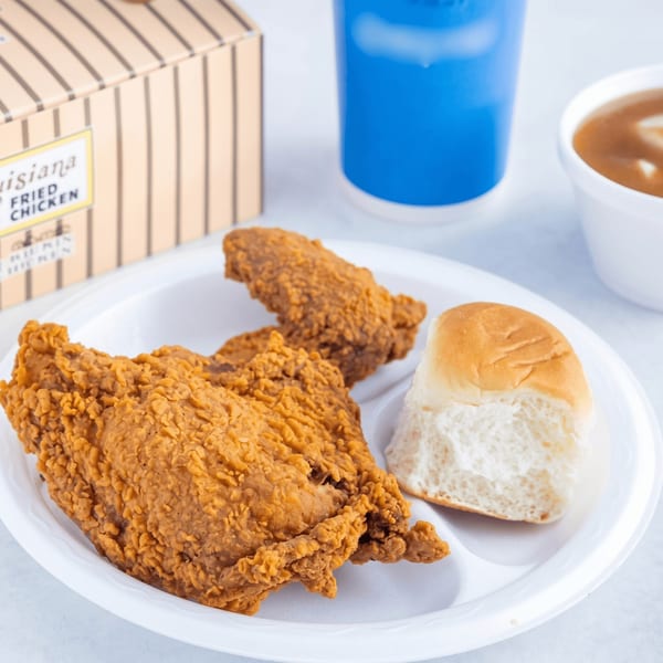 Two pieces of Louisiana Fried Chicken, a dinner roll, drink, and gravy on a white plate.